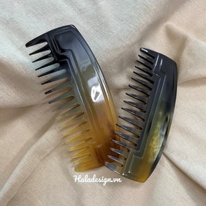 May include: Two tortoiseshell combs with black and brown patterns. The combs have a rounded shape and are made of a natural material.