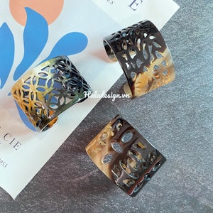 May include: Three black and brown tortoise shell bracelets with intricate cut-out designs. The bracelets are stacked on top of each other.