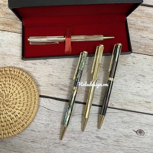 May include: Set of four pens with gold accents and iridescent mother-of-pearl inlays. The pens are in a black box with a red interior.