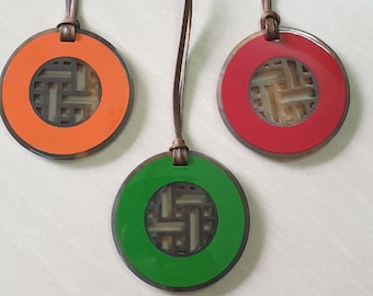 May include: Three round pendants with brown cords. The pendants are made of wood with a carved design in the center. The pendants are orange, red, and green.