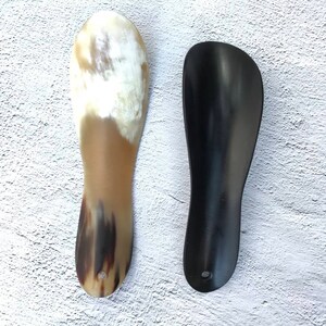 May include: Two shoe horns, one made of brown and black horn and one made of black plastic.