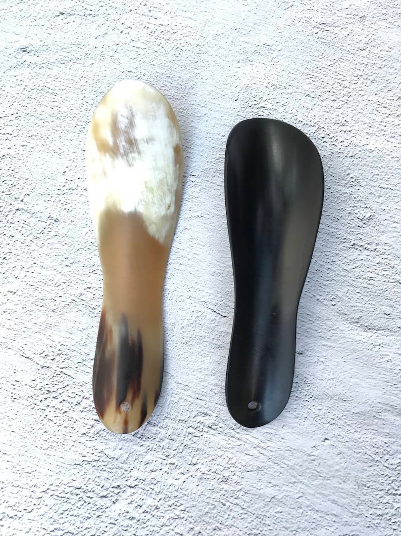 May include: Two shoe horns, one made of brown and black horn and one made of black plastic.