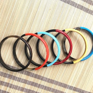 Op de afbeelding: Zes kleurrijke armbanden met zwarte en witte hoornaccenten. De armbanden zijn op elkaar gestapeld en zijn gerangschikt in een regenboogpatroon. De kleuren zijn blauw, rood, geel en zwart.