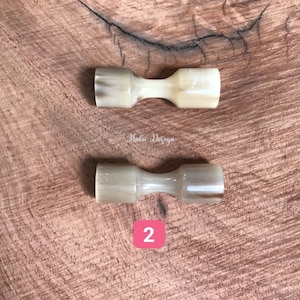 May include: Two natural horn handled butter knives on a wooden surface. The knives are a light beige color with brown streaks. The number "2" is written in red on a white background.
