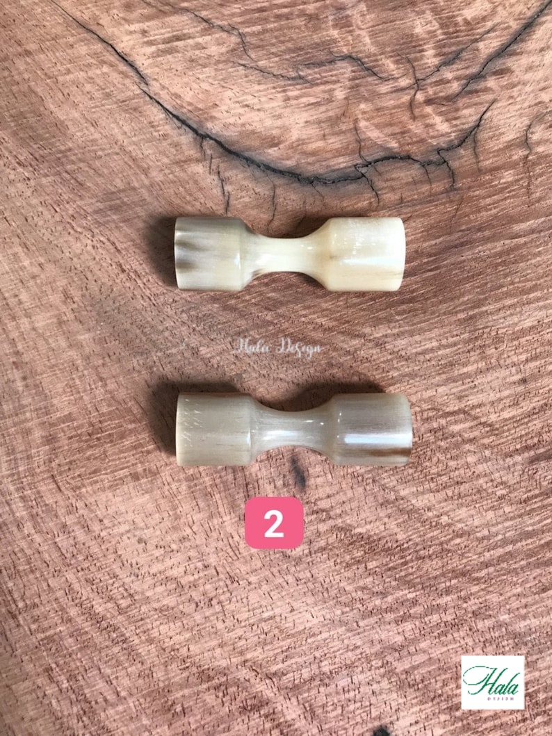 May include: Two natural horn handled butter knives on a wooden surface. The knives are a light beige color with brown streaks. The number "2" is written in red on a white background.