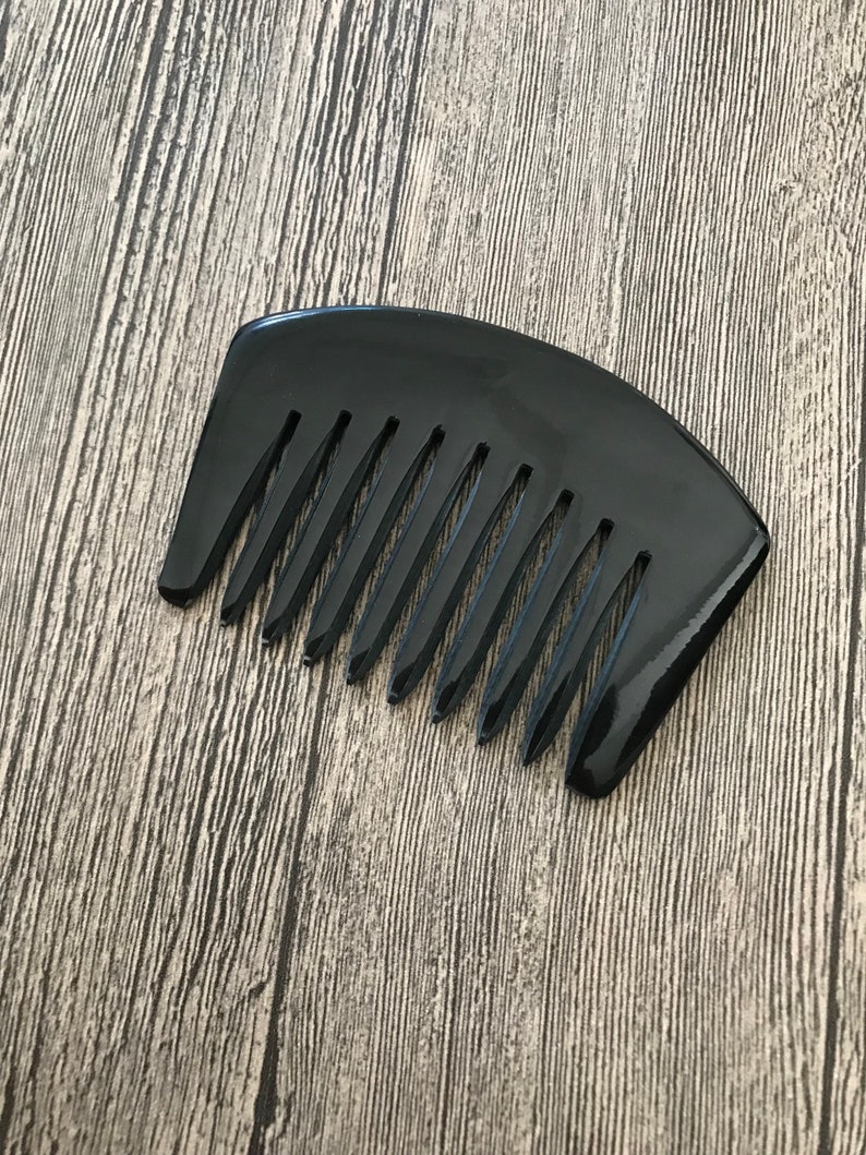 K&ouml;nnte beinhalten: Ein schwarzer Kamm mit breiten Z&auml;hnen und einem gebogenen Griff. Der Kamm ist aus einem gl&auml;nzenden, glatten Material.