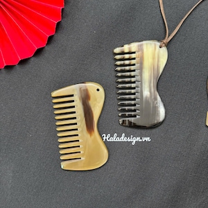 May include: Two horn combs with a natural, marbled appearance. One comb is attached to a brown cord. The combs have a curved handle and fine teeth. The text "Haladesign.vn" is visible on the image.