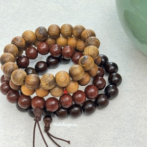 May include: Three wooden beaded bracelets stacked on top of each other. The top bracelet is light brown with dark brown streaks, the middle bracelet is dark red, and the bottom bracelet is dark brown. The bracelets are tied together with a brown string.