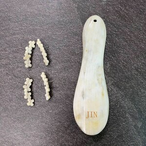 May include: Two pairs of white flower-shaped earrings and a white, oval-shaped, wooden tool with the word "JIN" engraved on it.