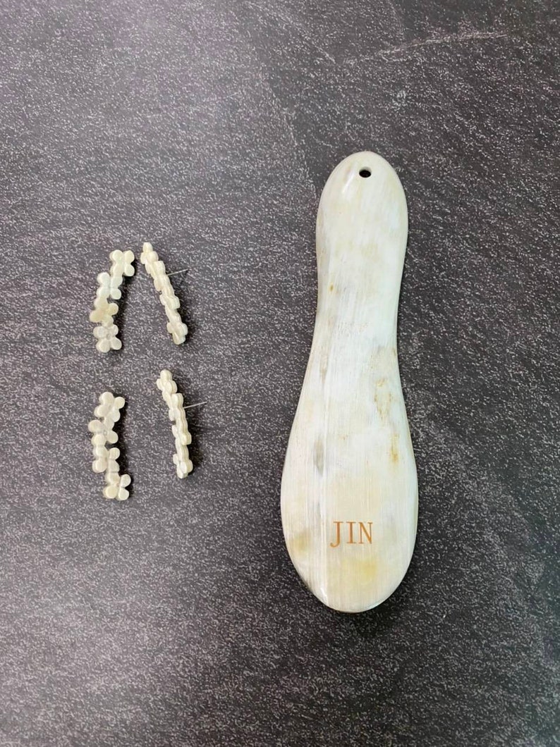May include: Two pairs of white flower-shaped earrings and a white, oval-shaped, wooden tool with the word "JIN" engraved on it.