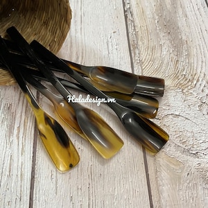 Puede incluir: Un juego de siete cueros de zapatos de cuerno marrón y negro. Los cueros de zapatos están dispuestos en forma de abanico sobre una superficie de madera clara.