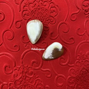 May include: Two white and brown teardrop-shaped decorative pieces on a red background with a floral pattern.