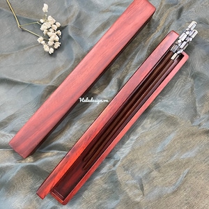 May include: A set of chopsticks in a red wooden box. The chopsticks have a silver design and are in a red wooden box.