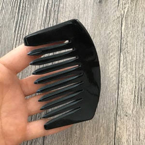 K&ouml;nnte beinhalten: Ein schwarzer Plastikkamm mit einem gebogenen Griff und breiten Z&auml;hnen.