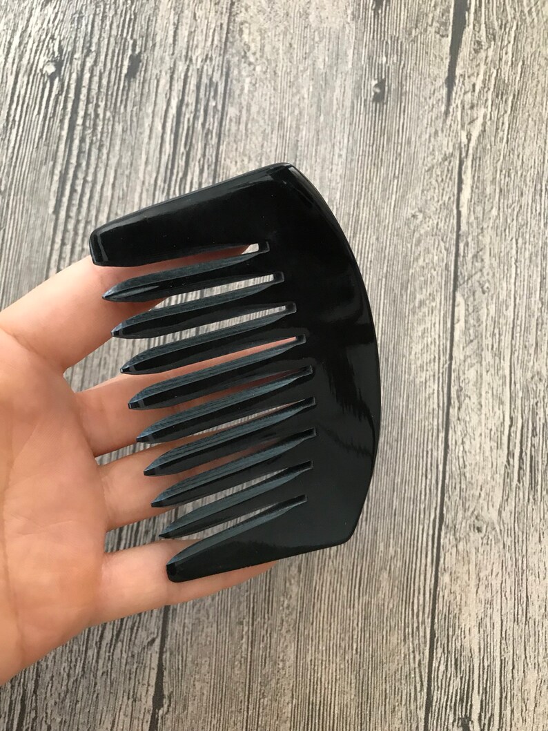 K&ouml;nnte beinhalten: Ein schwarzer Plastikkamm mit einem gebogenen Griff und breiten Z&auml;hnen.