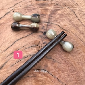 May include: A set of two pairs of chopsticks with decorative brown and white tips. The chopsticks are made of dark wood and are resting on a wooden surface. The number "1" is written on a pink square.