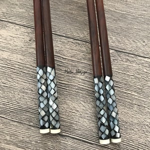 May include: Set of four brown wooden chopsticks with decorative mother-of-pearl tips. The tips are a mosaic of small, iridescent, gray and white squares.