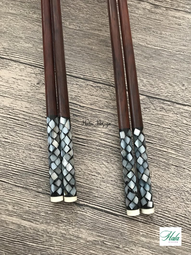 May include: Set of four brown wooden chopsticks with decorative mother-of-pearl tips. The tips are a mosaic of small, iridescent, gray and white squares.