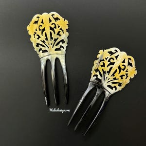 May include: Two decorative hair combs. Each comb has a yellow and white filigree design at the top, with three black prongs. The combs are set against a dark background. The text "Haladesign.vn" is visible.