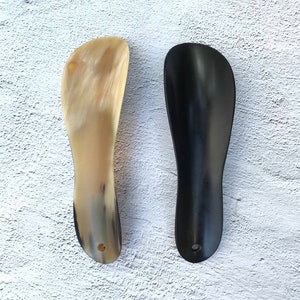 May include: Two shoe horns, one made of brown horn and one made of black horn.