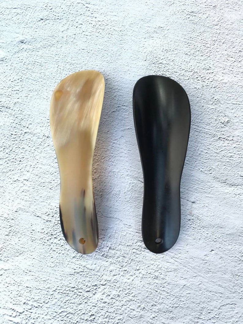 May include: Two shoe horns, one made of brown horn and one made of black horn.