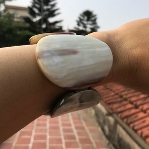 May include: A white and brown horn bracelet with a smooth, rounded surface. The bracelet is made of natural horn and has a unique, organic pattern.