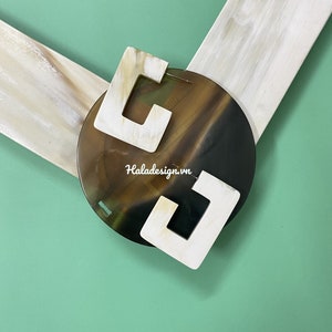 May include: Two white, square-shaped, open-frame earrings with a brown and black tortoiseshell background. The earrings are made of a natural material and have a unique, organic look.
