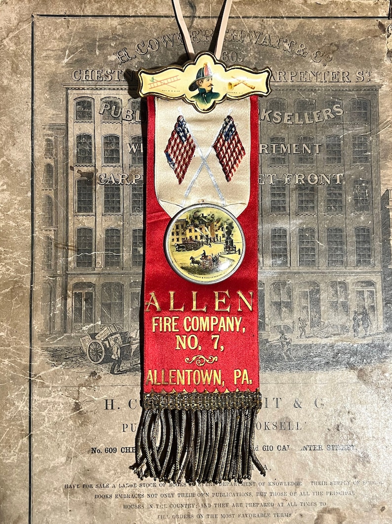 May include: A vintage red ribbon with gold fringe, featuring the text "ALLEN FIRE COMPANY, NO. 7, ALLENTOWN, PA." and a circular emblem with a horse-drawn carriage. The ribbon also displays two crossed American flags and a firefighter illustration.