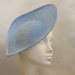Peut inclure: Un chapeau fascinateur bleu clair avec un large bord asymétrique et une finition en tissu tissé texturé. Le chapeau présente une bordure unie et lisse le long de tout le bord, créant une silhouette nette et définie pour cette coiffe.