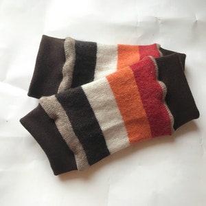 Può includere: Un paio di scaldagambe a righe marroni e bianche con righe arancioni e rosse. Gli scaldagambe sono realizzati in un tessuto morbido e lavorato a maglia.