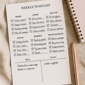 May include: A white weekly to-do list with checkboxes, categories like Work, Home, and Health, and a rose gold pen. A pink spiral notebook is in the background. The list includes tasks such as "Finish report" and "Go to gym."
