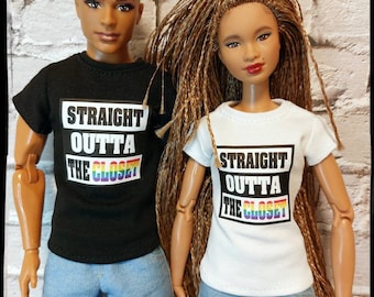 Puede incluir: Dos muñecas con camisetas y vaqueros azules posan frente a una pared de ladrillos. La camiseta negra lleva la frase "STRAIGHT OUTTA THE CLOSET" con un diseño de arcoíris. La camiseta blanca tiene el mismo texto y diseño.
