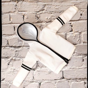 Peut inclure: Sweat-shirt &agrave; capuche blanc avec des rayures noires sur les manches. Le sweat-shirt est pos&eacute; &agrave; plat sur un mur en briques blanches.