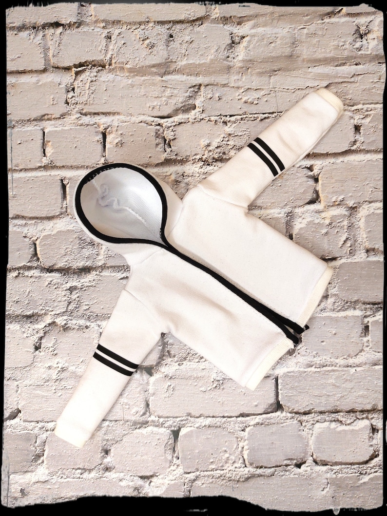 Peut inclure: Sweat-shirt &agrave; capuche blanc avec des rayures noires sur les manches. Le sweat-shirt est pos&eacute; &agrave; plat sur un mur en briques blanches.