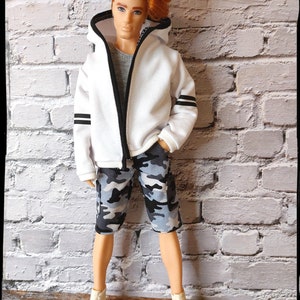 Peut inclure: Un sweat &agrave; capuche blanc avec des bordures noires et des rayures noires sur les manches. Le sweat est zipp&eacute; et le mannequin porte un short camouflage et des baskets blanches.