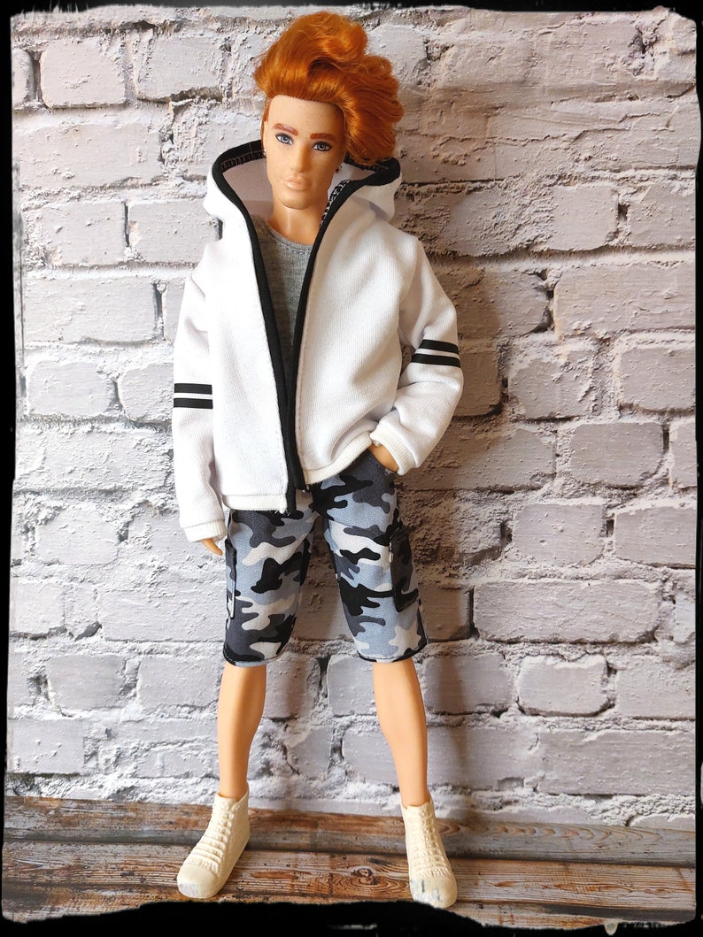 Peut inclure: Un sweat &agrave; capuche blanc avec des bordures noires et des rayures noires sur les manches. Le sweat est zipp&eacute; et le mannequin porte un short camouflage et des baskets blanches.