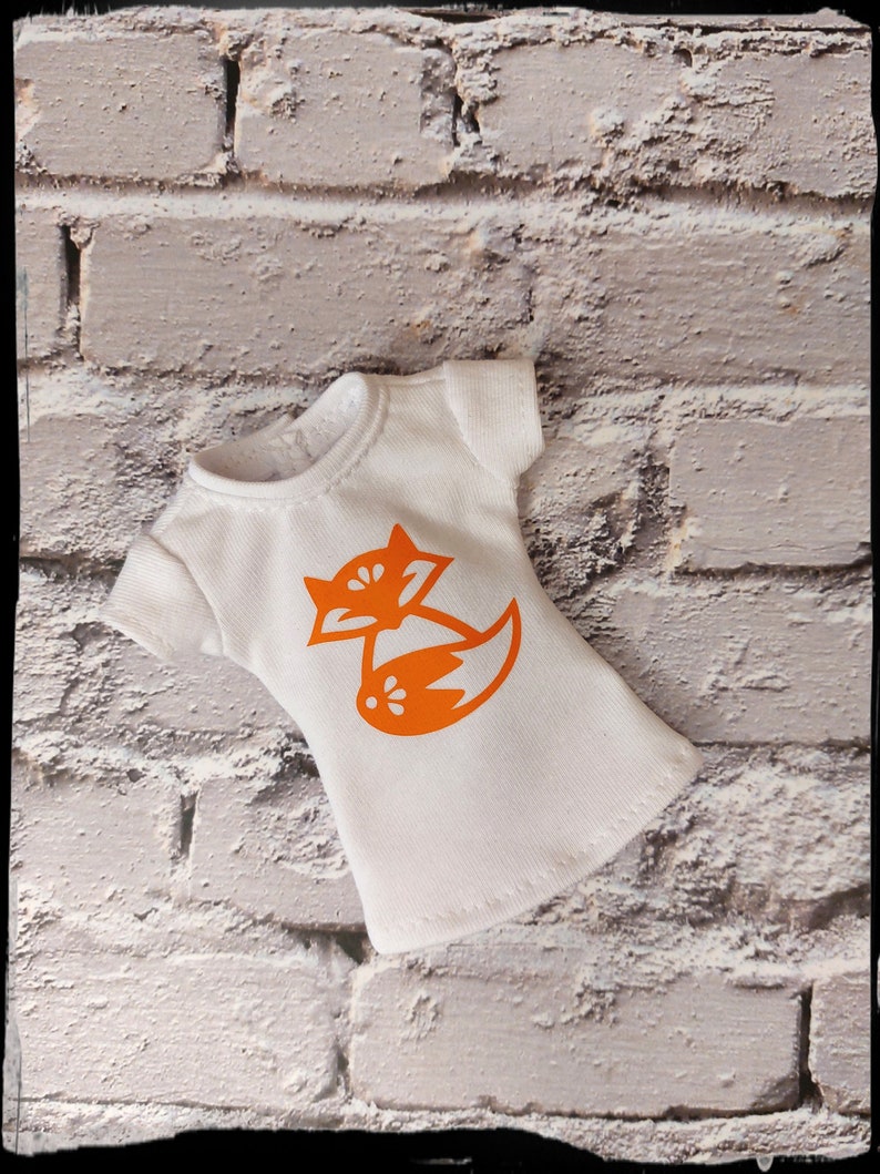 May include: White t-shirt with an orange fox graphic. The fox is curled up with its tail wrapped around its body.