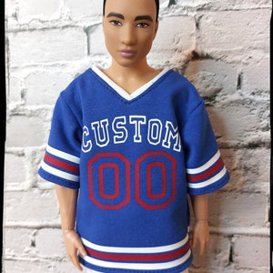 Peut inclure: Maillot bleu avec des rayures blanches et rouges, avec le mot "CUSTOM" et le numéro "00" en rouge.