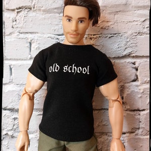 May include: A black t-shirt with the text "old school" in white lettering. The shirt is being worn by a doll with brown hair and a light brown complexion.