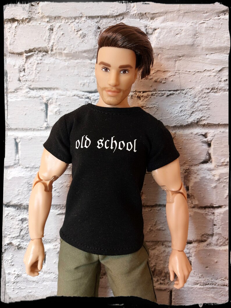 May include: A black t-shirt with the text "old school" in white lettering. The shirt is being worn by a doll with brown hair and a light brown complexion.