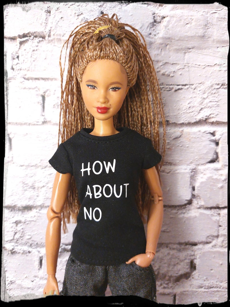 May include: A black t-shirt with the text "HOW ABOUT NO" in white lettering. The shirt is being worn by a doll with brown hair and a light brown complexion.