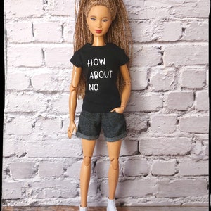 May include: A doll wearing a black t-shirt with the text "HOW ABOUT NO" in white, denim shorts, and white sneakers. The doll has long brown hair and is standing in front of a white brick wall.