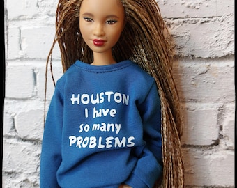 Może przedstawiać: Lalka z długimi brązowymi warkoczami ubrana w niebieską bluzę z napisem "HOUSTON I have so many PROBLEMS" i niebieskie dżinsy.