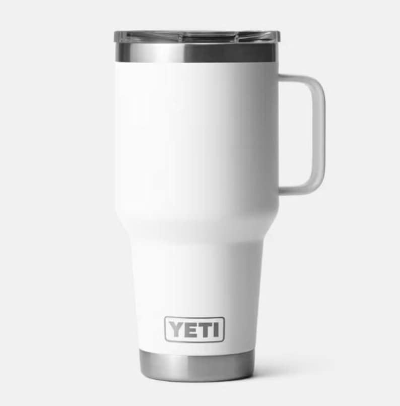 Pu&ograve; includere: Tazza da viaggio isolante bianca con manico e bordo e base argentati. La tazza ha il marchio "YETI" in un riquadro rettangolare sul davanti. Progettata per mantenere le bevande calde o fredde.