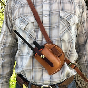 May include: A brown leather holster with a stitched design, worn on a person's shoulder, for a two-way radio with a black antenna.