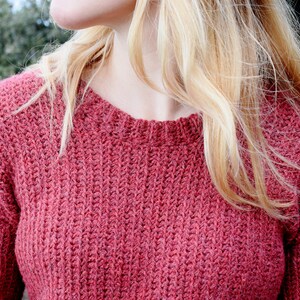 May include: A close-up of a woman wearing a red knitted sweater. The sweater has a textured, ribbed pattern.