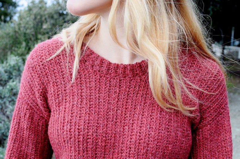 May include: A close-up of a woman wearing a red knitted sweater. The sweater has a textured, ribbed pattern.