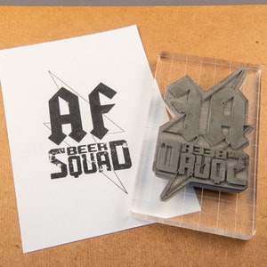 May include: A clear acrylic stamp with a black rubber design. The design says "AF Beer Squad" in a bold, stylized font.