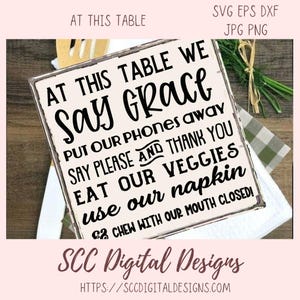 May include: A white sign with black text that reads "At this table we say grace, put our phones away, say please and thank you, eat our veggies, use our napkin, & chew with our mouth closed!" The sign has a distressed look and is on a checkered background.