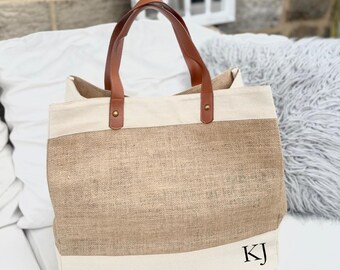 May include: A beige and tan tote bag with brown leather handles. The bag features a wide tan stripe across the middle and a white stripe at the top and bottom. The initials "KJ" are printed in black on the lower right corner.
